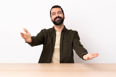 Masada sakallı, beyaz bir adam sunuyor ve davet ediyor..