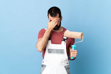 Yetişkin ressam, izole edilmiş mavi arka planda, gözleri elleriyle kapatıyor.