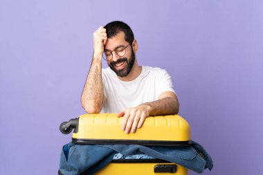 Bir bavul dolusu elbisesi olan Kafkasyalı gezgin, izole edilmiş mor arka planda gülüyor.