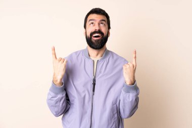 Sakallı, ceketli, soyutlanmış arka planı olan beyaz bir adam şaşırmış ve yukarı bakıyor.