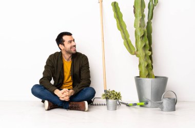 Bahçıvan içeride yerde oturuyor. Yan tarafa bakıyor ve gülümsüyor.