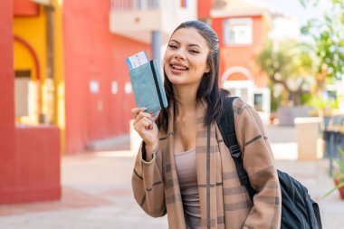Açık havada elinde mutlu bir ifadeyle pasaport tutan genç ve güzel bir kadın.