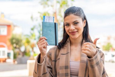 Dışarıda pasaportu olan genç ve güzel bir kadın. Başparmakları havada. Çünkü iyi bir şey oldu.