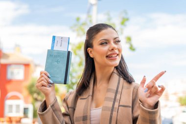 Pasaportu elinde tutan genç ve güzel bir kadın bir ürün sunmak için yan tarafı işaret ediyor.