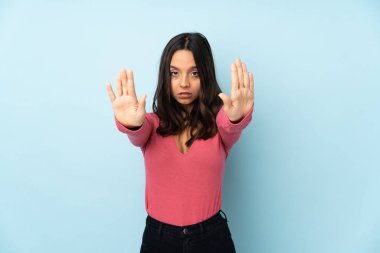 Genç melez kadın mavi arka planda izole edilmiş. Durma hareketi yapıyor ve hayal kırıklığına uğruyor.