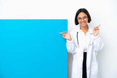 Beyaz arka planda izole edilmiş büyük bir pankartla genç melez doktor kadın parmak uçlarını işaret ediyor ve mutlu.
