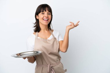 Tepsisi beyaz arka planda izole edilmiş genç garson, davet edilmek için ellerini yana uzatıyor.