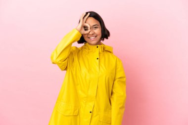 İzole edilmiş arka planda yağmura dayanıklı bir ceket giyen genç Latin kadın parmaklarıyla işaret veriyor.
