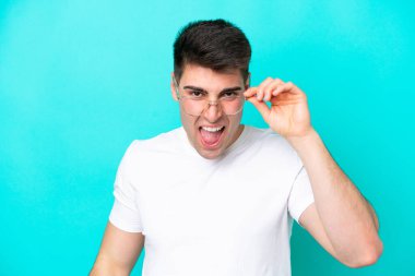 Mavi arka planda gözlüklü ve hayal kırıklığına uğramış bir beyaz adam.