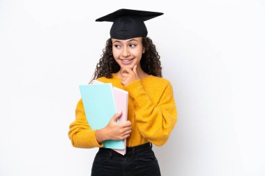 Arap üniversite mezunu kadın elinde kitaplarla beyaz arka planda izole bir şekilde yan tarafa bakıyor ve gülümsüyor.