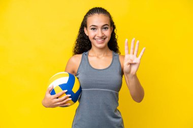 Young woman playing volleyball isolated on yellow background happy and counting four with fingers