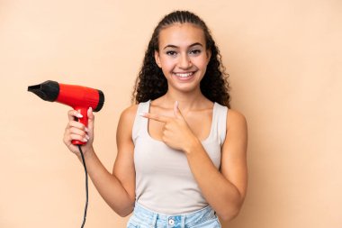 Elinde bej arka planda izole edilmiş bir saç kurutma makinesi tutan genç bir kadın.