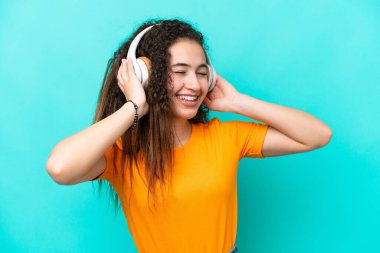 Genç Arap kadın mavi arka planda izole edilmiş müzik dinliyor ve şarkı söylüyor.