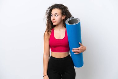 Genç Arap spor kadını yoga derslerine giderken beyaz arka planda izole edilmiş bir minder tutuyor ve yan tarafa bakıyor.