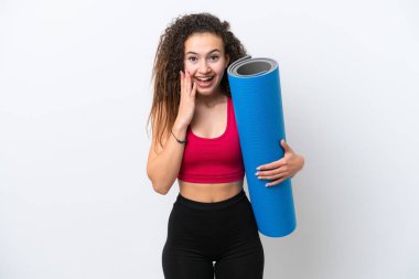 Genç Arap spor kadını yoga derslerine giderken beyaz arka planda yalıtılmış ve şok olmuş bir yüz ifadesiyle bir minder tutuyor.