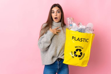 Pembe arka planda izole edilmiş plastik şişelerle dolu bir çanta taşıyan beyaz bir kadın şaşırmış ve şok olmuştu.