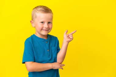 Küçük Rus çocuk sarı arka planda izole edilmiş, parmağını yana doğru gösteriyor.