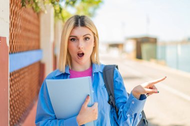 Açık havada genç ve güzel bir bayan öğrenci şaşırmış ve işaret ediyor.