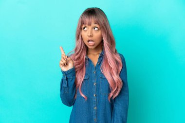 Mavi arka planda izole edilmiş pembe saçlı melez bir kadın.