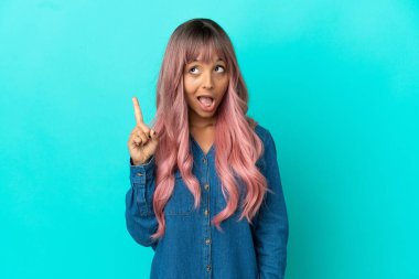 Mavi arka planda izole edilmiş pembe saçlı melez bir kadın çözümü bulmak için parmağını kaldırıyor.