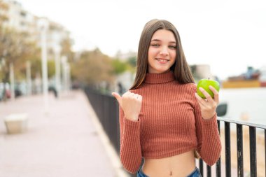 Açık havada elmalı ergen bir kız bir ürünü sunmak için yan tarafı işaret ediyor.