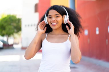 Genç Afrikalı Amerikalı kadın açık havada müzik dinliyor.