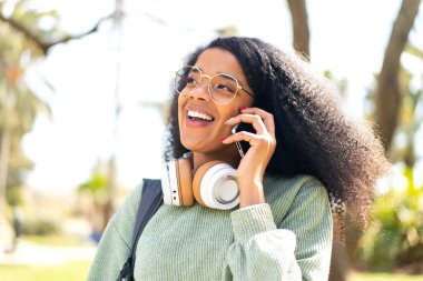 Açık havada cep telefonu kullanan genç Afrikalı Amerikalı kadın.