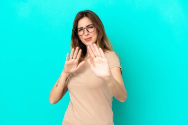 Mavi arka planda izole edilmiş genç beyaz kadın ellerini öne uzatıyor.