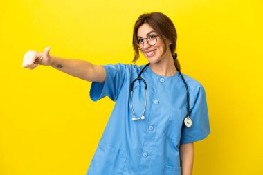 Doktor kadın, sarı arka planda izole edilmiş bir şekilde baş parmak hareketi yapıyor.