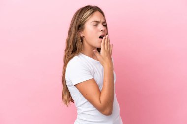 Pembe arka planda izole edilmiş küçük beyaz kız esniyor ve ağzını eliyle açık tutuyor.