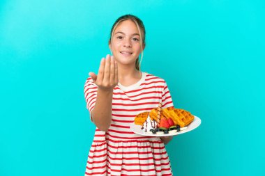 Mavi arka planda izole edilmiş waffle 'ları tutan küçük beyaz bir kız benimle gelmek için davet ediyor. Gelmene sevindim.