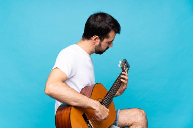 Mavi arka planda gitar çalan genç bir adam.