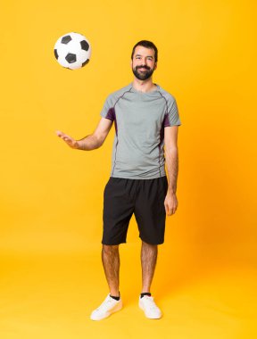 İzole edilmiş sarı arka planda bir futbolcunun tam boy çekimi.