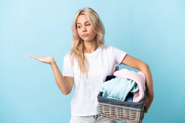 Mavi arka planda izole edilmiş çamaşır sepetini tutan genç Rus kadın telif alanını şüpheyle tutuyor