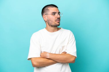 Mavi arka planda izole edilmiş genç beyaz adam yan tarafa bakıyor.