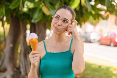 Açık havada kornet dondurması olan genç ve güzel bir kadın. Şüpheleri var ve kafası karışmış bir yüz ifadesi var.
