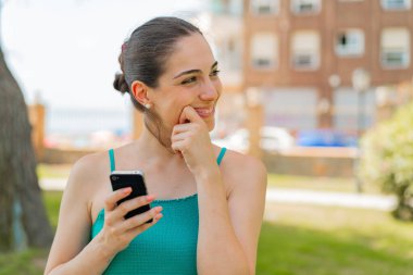 Dışarıda cep telefonu kullanan genç ve güzel bir kadın bir fikir üretiyor ve ona bakıyor.