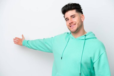 Beyaz arka planda soyutlanmış beyaz tenli genç adam davet edilmek için ellerini yana uzatıyor.