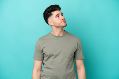 Kafkasyalı genç adam mavi arka planda izole edilmiş bir şekilde yukarı bakarken bir fikir düşünüyor.