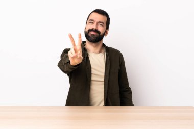 Masada sakallı, gülümseyen ve zafer işareti gösteren beyaz bir adam..