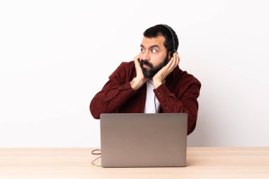 Tele pazarlamacı beyaz bir adam kulaklıkla ve bilgisayarla çalışıyor hayal kırıklığına uğramış ve kulakları tıkalı..