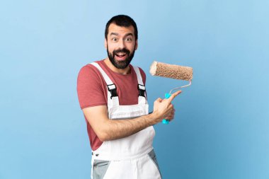 Yetişkin ressam, izole edilmiş mavi arka planda şaşırmış ve işaret ediyor.