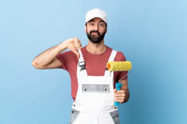 Yetişkin ressam mavi arkaplan üzerinde negatif ifade ile baş parmak aşağı gösteren