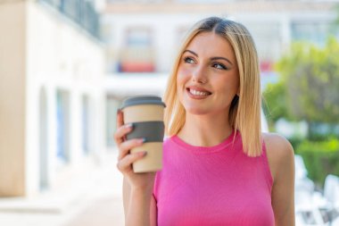 Genç, güzel, sarışın bir kadın gülümserken yukarı bakıyor.