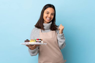 Pasta şefi mavi arka planda büyük bir pasta tutuyor ve gülüyor..