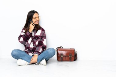 Genç bir bayan öğrenci yerde oturuyor ve cep telefonuyla birileriyle sohbet ediyor.