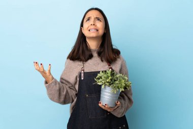 Genç, esmer, melez bir kadın, mavi arka planda bir bitki tutuyor..