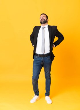 Bir iş adamının izole edilmiş sarı arka planda gösterdiği çabadan dolayı sırt ağrısından muzdarip olduğu uzun bir çekim.