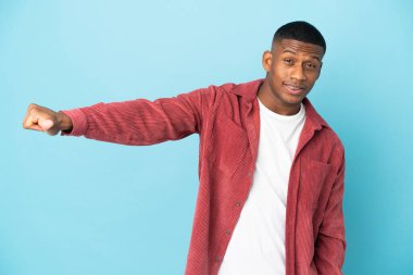 Mavi arka planda izole edilmiş genç latin adam baş parmak işareti yapıyor.