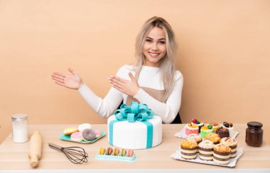 Masasında büyük bir pasta olan ergen pasta şefi davet etmek için ellerini yana uzatıyor.